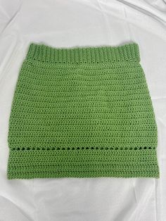 a green crocheted skirt laying on top of a white sheet with holes in it