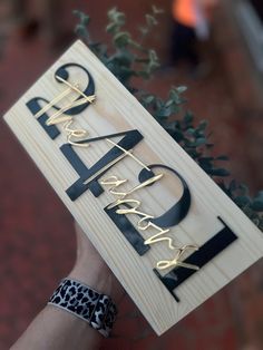 a person holding up a wooden sign that says happy birthday with black and gold letters