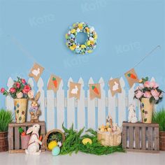 an easter scene with bunnies, eggs and flowers on the table next to a white picket fence