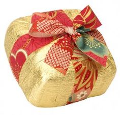 a gold and red wrapped gift box with a bow on the top, isolated against a white background