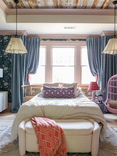 a bed sitting in a bedroom next to a window with two hanging lamps above it