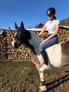 a woman riding on the back of a brown and white horse next to a pile of logs