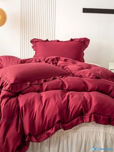 a bed with red sheets and pillows on top of it in a white room next to a lamp