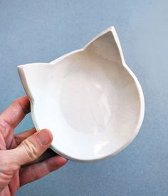 a person holding a white cat shaped bowl in their left hand on a blue surface