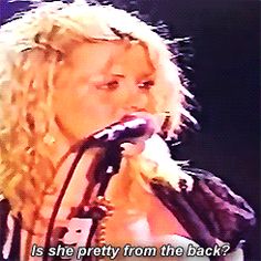 a woman singing into a microphone with the words, is she pretty from the back?