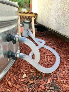 a hose connected to the side of a metal tank on top of mulchy ground