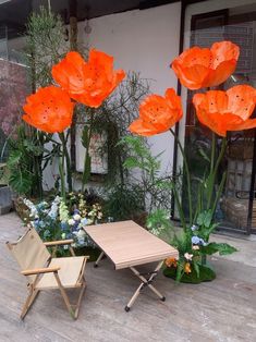 two chairs and a table in front of some orange flowered plants on the ground