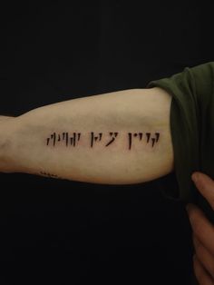 a person with a tattoo on their arm that has writing in hebrew and english letters