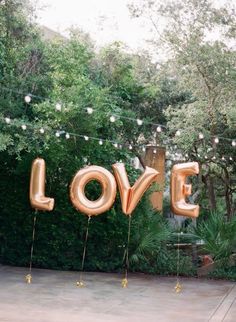 the letters love spelled out in gold foil are hanging from string lights and surrounded by greenery