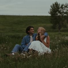 a man and woman are sitting in the grass looking into each others eyes as they laugh