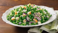 a white bowl filled with peas, onions and carrots on top of a wooden table