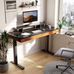 a desk with a computer on it in front of a window and a potted plant