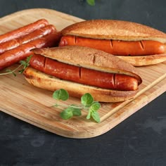 two hotdogs on buns sitting on a cutting board next to each other