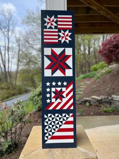 an american flag quilt hanging on a wooden post in front of a covered area with trees and bushes