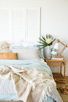 a bed with white and blue sheets, pillows and blankets on top of it in a bedroom