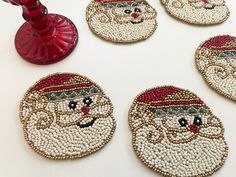 four coasters with beaded santa claus faces on them and a red candle holder