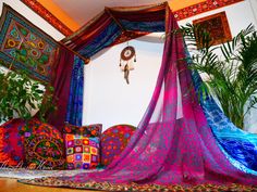 a canopy bed covered in colorful blankets and pillows next to a potted palm tree