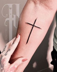 a person holding their arm with a cross tattoo on it