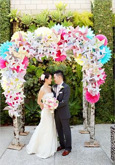 a bride and groom standing under a colorful paper arch