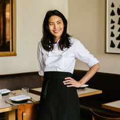 a woman standing in front of a table with plates and glasses on it, wearing a white shirt and black skirt