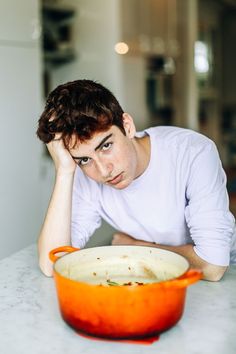 a man sitting at a table with an orange casserole in front of him