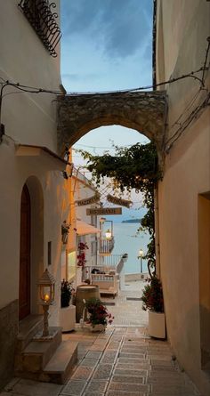 an alley way leading to the beach with flowers and umbrellas hanging from it's sides