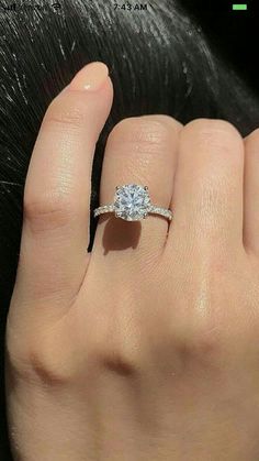 a woman's hand with a diamond ring on top of her finger and the other hand holding an engagement ring