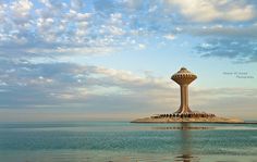 an island with a water tower in the middle of it, surrounded by blue sky and clouds