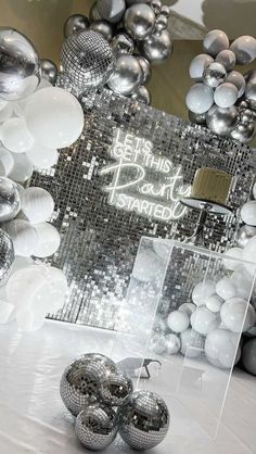 a table topped with lots of silver and white balloons in front of a mirror frame