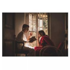 two people sitting at a table in front of a window, one reading a book