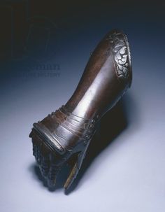 an old wooden shoe with metal decoration on the top and bottom, sitting on a blue surface