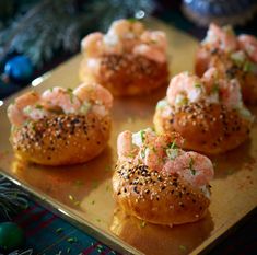 small bagels with shrimp on them are sitting on a gold tray next to christmas decorations