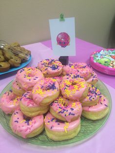 a plate full of pink frosted donuts with sprinkles on them