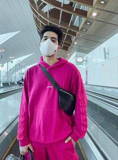 a man wearing a face mask and carrying a handbag while standing in front of an escalator