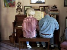 two people are sitting at a piano in the living room and one person is reading