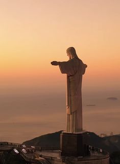 the statue of jesus is overlooking the ocean at sunset