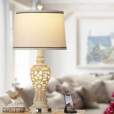 a table lamp sitting on top of a wooden table next to a phone and flowers