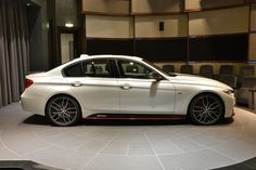 a white car is on display in a room with gray chairs and a round table