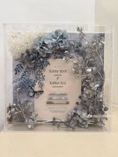 a wedding card in a clear box with flowers and leaves