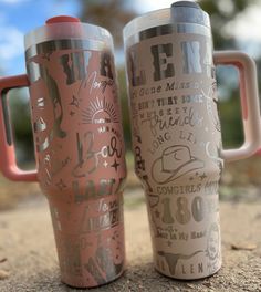 two travel mugs sitting next to each other on the ground