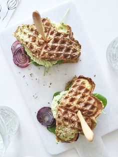 two waffle sandwiches with lettuce, tomato and onion on them sitting on a cutting board