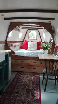 a bed sitting in the middle of a room next to a table and chair with a rug on top of it