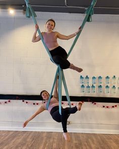 two women are doing aerial acrobatic tricks in a dance studio, one is holding on to the other's legs