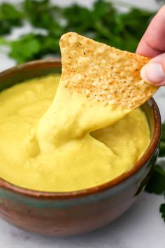 a hand dipping a tortilla chip into a bowl