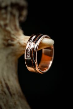 two wedding bands with diamonds on them sitting next to a piece of driftwood in front of a black background