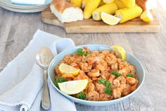 a bowl filled with shrimp next to corn on the cob and lemon wedges