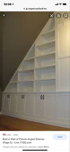 an empty room with white bookcases and wood flooring in front of a slanted wall