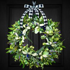 a green wreath with white flowers and greenery hanging on a black front door frame