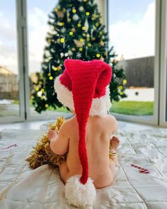 a baby wearing a santa hat sitting on top of a bed next to a christmas tree