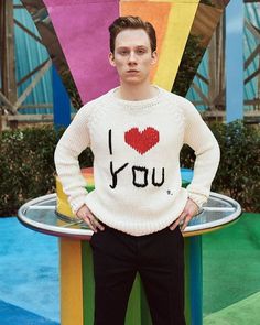 a young man standing in front of a rainbow colored sculpture with the words i love you written on it